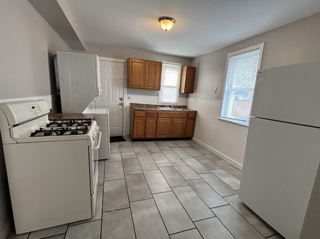 kitchen featuring white appliances, brown cabinetry, a sink, light tile patterned floors, and baseboards
