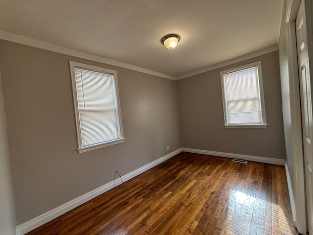 spare room featuring dark wood-type flooring, baseboards, and crown molding