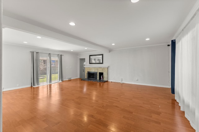 unfurnished living room featuring light wood finished floors, recessed lighting, a tile fireplace, baseboards, and ornamental molding