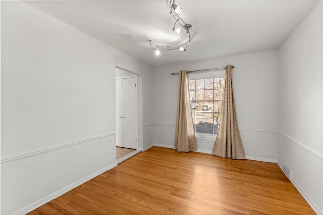 unfurnished room featuring light wood-type flooring, baseboards, and rail lighting
