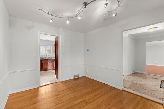 unfurnished room with light wood-style flooring, baseboards, a sink, and ornamental molding