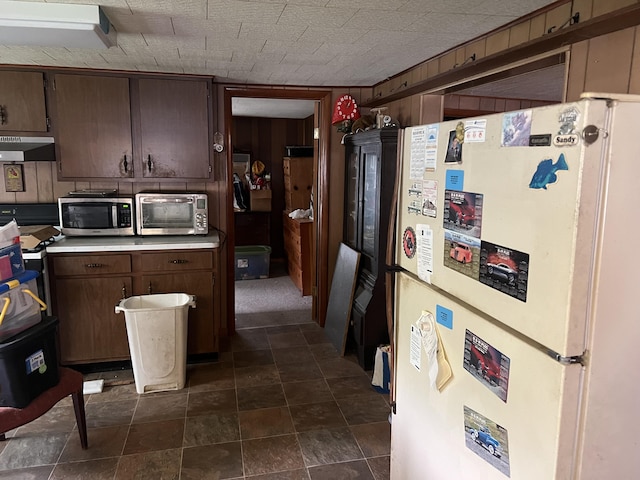 kitchen featuring freestanding refrigerator, stainless steel microwave, under cabinet range hood, dark brown cabinets, and light countertops