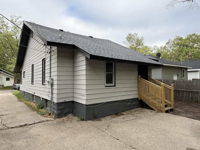 view of side of home featuring fence and a shingled roof