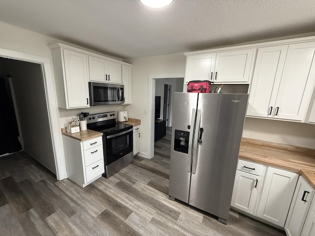 kitchen featuring appliances with stainless steel finishes, wooden counters, white cabinetry, and wood finished floors