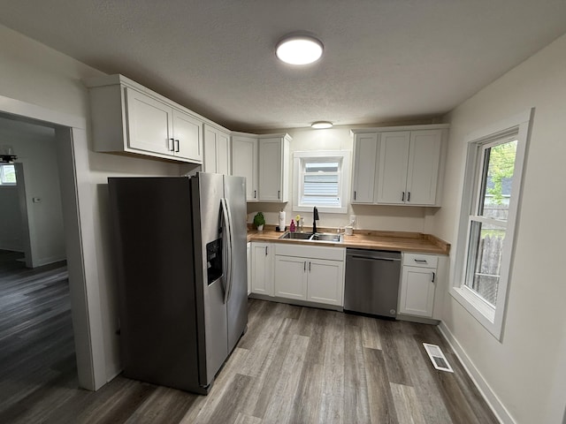 kitchen featuring stainless steel appliances, a sink, dark wood-type flooring, a textured ceiling, and white cabinets