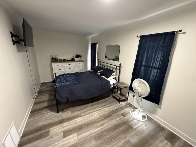 bedroom featuring wood finished floors, crown molding, and baseboards