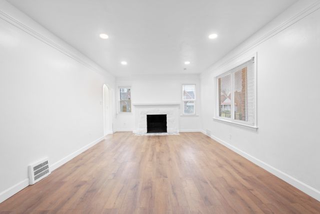 18711 Indiana St, Detroit, MI 48221 - unfurnished living room with wood finished floors, baseboards, recessed lighting, a fireplace with flush hearth, and arched walkways