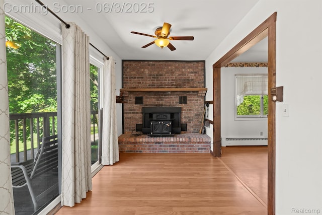 7109 Lake Shore Dr, Chelsea, MI 48118 - unfurnished living room with a baseboard radiator, a ceiling fan, wood finished floors, and a wood stove