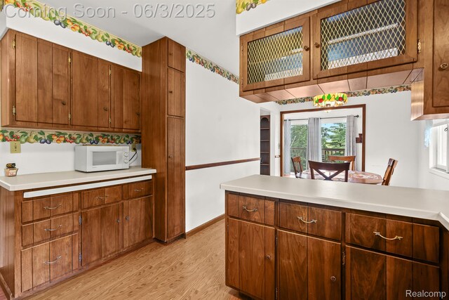 7109 Lake Shore Dr, Chelsea, MI 48118 - kitchen with white microwave, light wood-style floors, light countertops, a peninsula, and brown cabinets