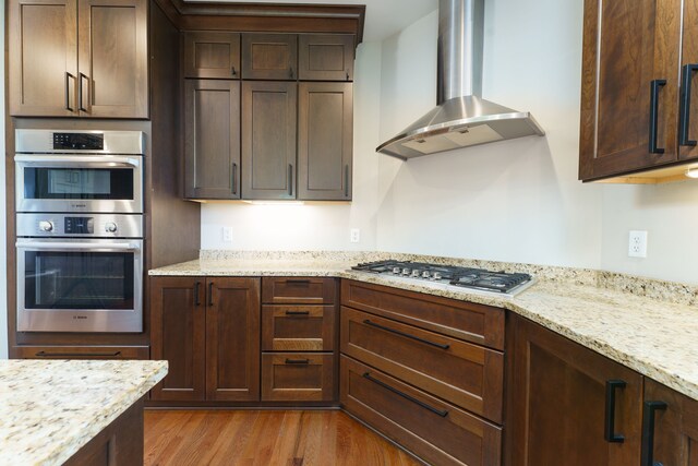 10408 Stoney Point Dr, South Lyon, MI 48178 - kitchen featuring wall chimney range hood, stainless steel appliances, wood finished floors, and light stone counters
