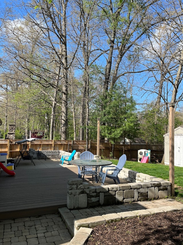 view of patio / terrace with a fenced backyard, a storage unit, a wooden deck, and an outbuilding