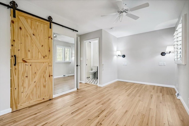 spare room featuring a barn door, a ceiling fan, and light wood-type flooring