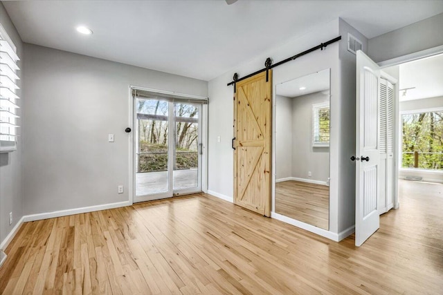 spare room with a barn door, light wood-style floors, healthy amount of natural light, baseboards, and recessed lighting