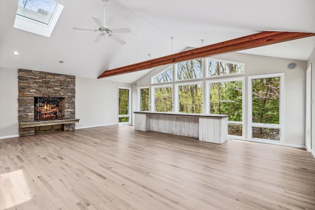 unfurnished living room with a skylight, a stone fireplace, light wood-style floors, a ceiling fan, and high vaulted ceiling