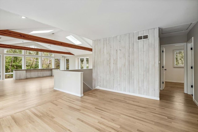 unfurnished living room with healthy amount of natural light, baseboards, wood finished floors, wooden walls, and a skylight