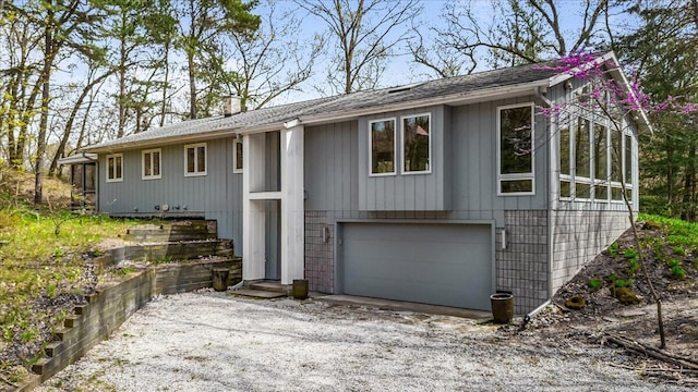 bi-level home with dirt driveway, a chimney, a garage, and roof with shingles
