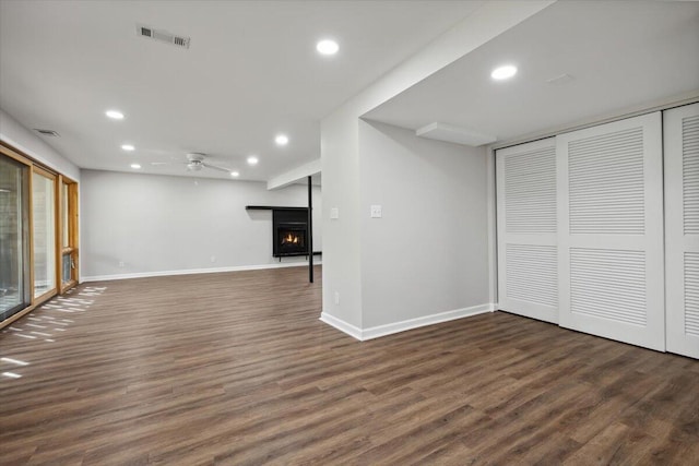 below grade area featuring recessed lighting, a lit fireplace, dark wood finished floors, baseboards, and ceiling fan