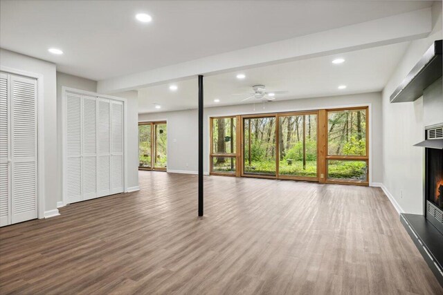 unfurnished living room with a warm lit fireplace, wood finished floors, baseboards, recessed lighting, and a ceiling fan