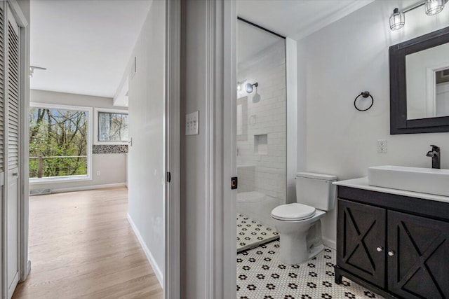 full bath with toilet, tiled shower, vanity, baseboards, and wood finished floors