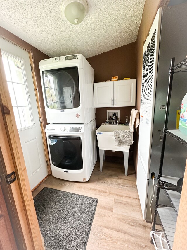 1076 N Lakeshore Rd, Harbor Beach, MI 48441 - clothes washing area with estacked washer and dryer, cabinet space, a textured ceiling, and light wood-style floors