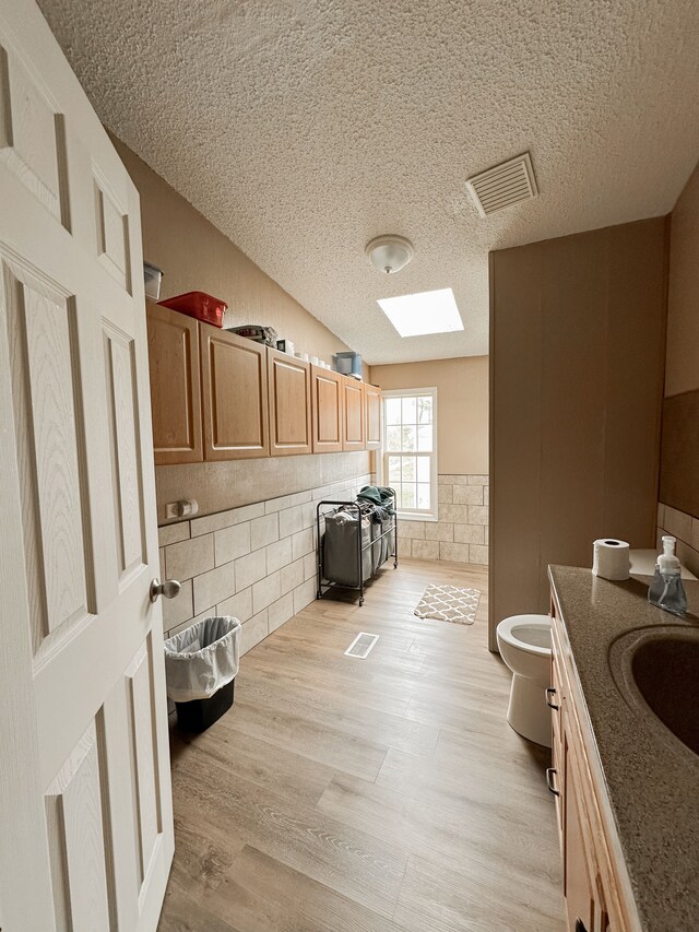 1076 N Lakeshore Rd, Harbor Beach, MI 48441 - laundry room featuring tile walls, a textured ceiling, a wainscoted wall, a skylight, and light wood-style floors
