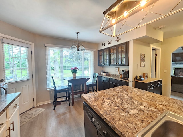 kitchen featuring a chandelier, dishwasher, light wood-style flooring, glass insert cabinets, and light stone countertops