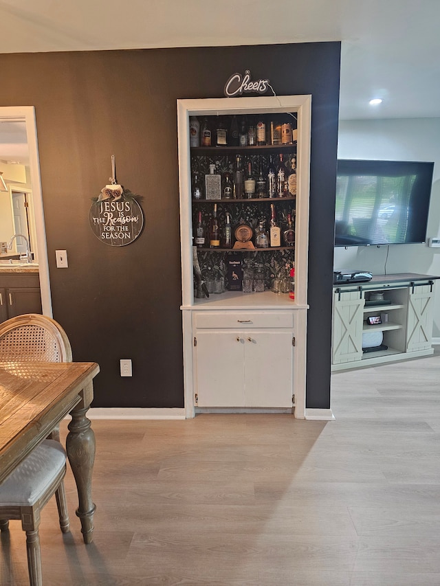 bar featuring light wood-style flooring, a sink, recessed lighting, and baseboards