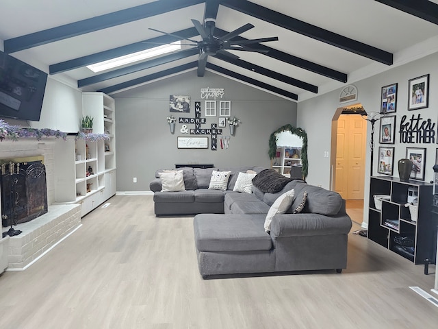 living area featuring a fireplace, arched walkways, wood finished floors, ceiling fan, and a skylight