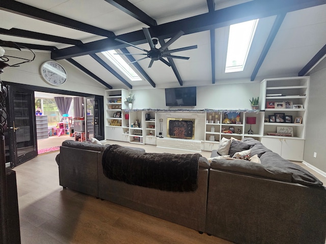 living room with ceiling fan, wood finished floors, a fireplace with raised hearth, and a skylight