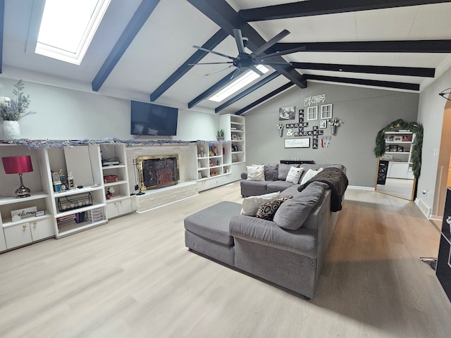 living room with a skylight, ceiling fan, wood finished floors, and a fireplace with raised hearth