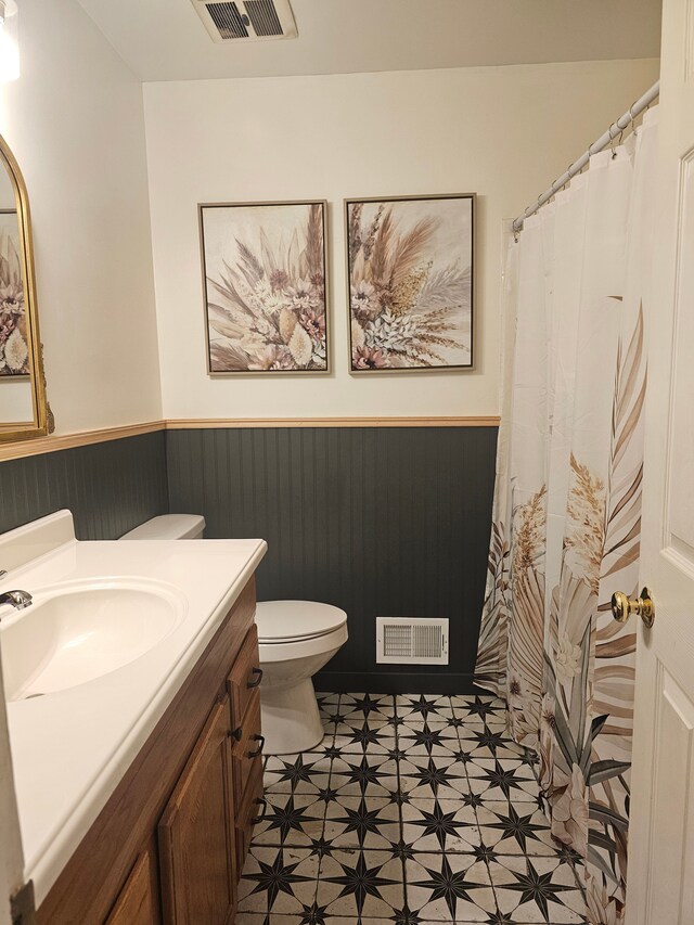 bathroom featuring a wainscoted wall, toilet, tile patterned floors, and vanity