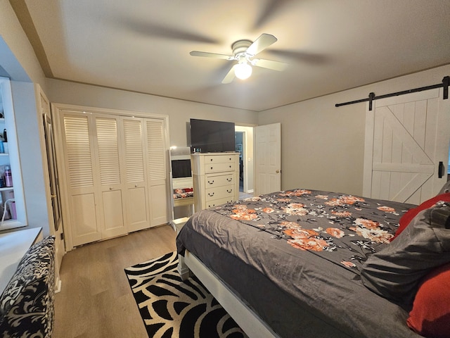 bedroom with a barn door, light wood-style floors, a closet, and ceiling fan