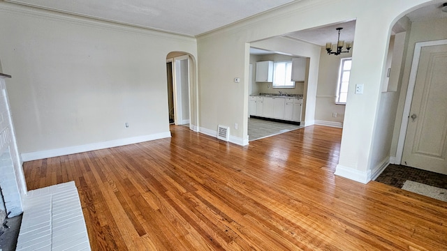 5790 Lakepointe St, Detroit, MI 48224 - unfurnished living room featuring arched walkways, crown molding, a chandelier, light wood-style flooring, and baseboards