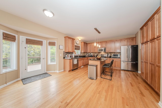 57677 Blossom Valley Trl, New Hudson, MI 48165 - kitchen with stainless steel appliances, a sink, light wood-type flooring, dark countertops, and a kitchen breakfast bar
