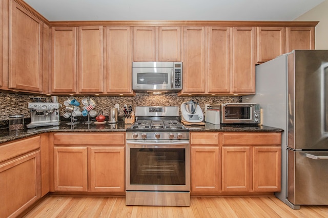 57677 Blossom Valley Trl, New Hudson, MI 48165 - kitchen featuring appliances with stainless steel finishes, light wood-style flooring, tasteful backsplash, and dark stone countertops