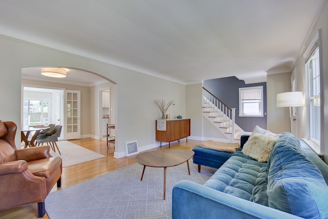 living area with arched walkways, stairs, wood finished floors, baseboards, and ornamental molding