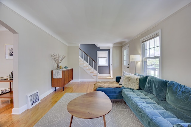 living area featuring stairs, light wood-style floors, healthy amount of natural light, and ornamental molding