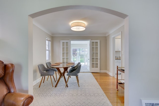 dining room featuring light wood-style flooring, arched walkways, baseboards, and french doors