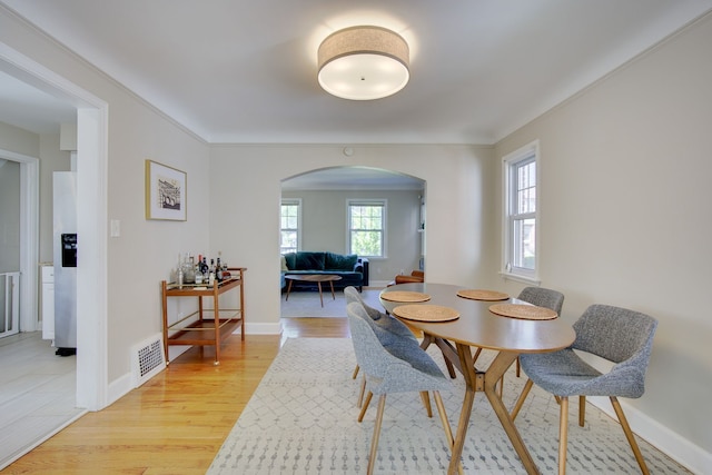 dining space featuring arched walkways, light wood-style flooring, and baseboards