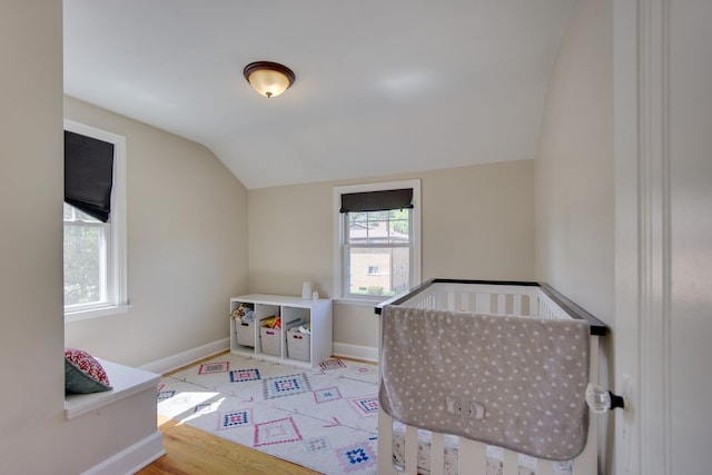 bedroom with lofted ceiling, baseboards, a crib, and wood finished floors