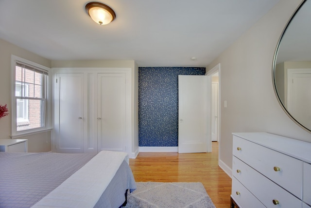 bedroom with wallpapered walls, light wood-style flooring, baseboards, and a closet