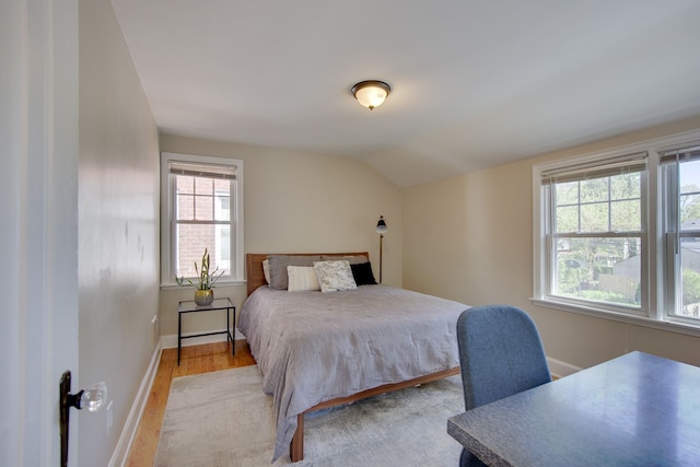 bedroom featuring light wood finished floors, baseboards, and lofted ceiling