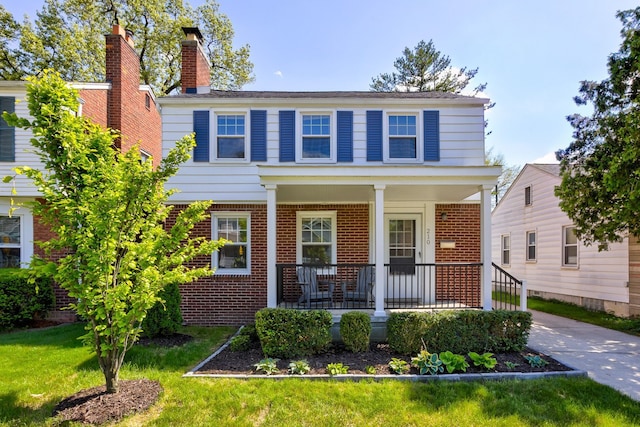view of front of house featuring brick siding, covered porch, a front lawn, and a chimney