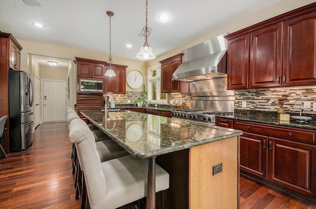 4181 Pavilion Ct, Fenton, MI 48430 - kitchen featuring wall chimney range hood, stainless steel appliances, a center island with sink, dark wood-style floors, and dark brown cabinets