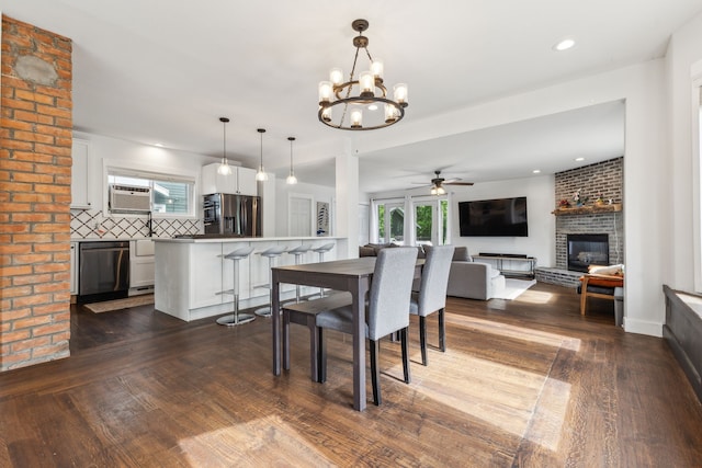 dining area featuring a brick fireplace, a ceiling fan, dark wood-style flooring, a chandelier, and recessed lighting