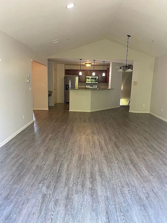 18203 Adri Cir, Walled Lake, MI 48390 - unfurnished living room featuring dark wood-style flooring, lofted ceiling, and baseboards