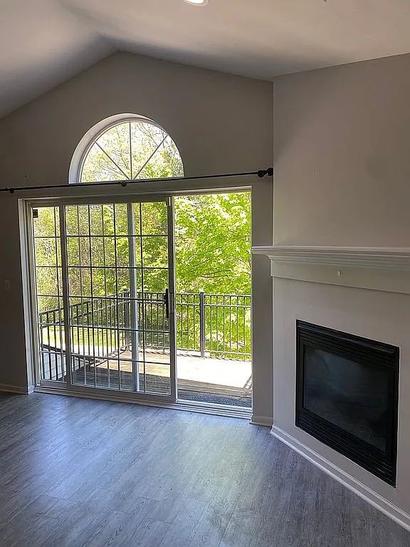 18203 Adri Cir, Walled Lake, MI 48390 - unfurnished living room with wood finished floors, lofted ceiling, a glass covered fireplace, and baseboards