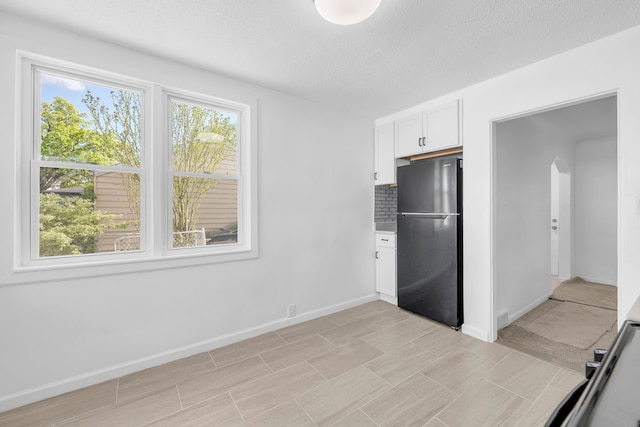 kitchen with freestanding refrigerator, arched walkways, white cabinetry, a textured ceiling, and tasteful backsplash