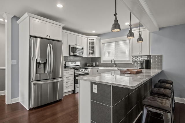 kitchen featuring appliances with stainless steel finishes, a peninsula, a breakfast bar, recessed lighting, and baseboards
