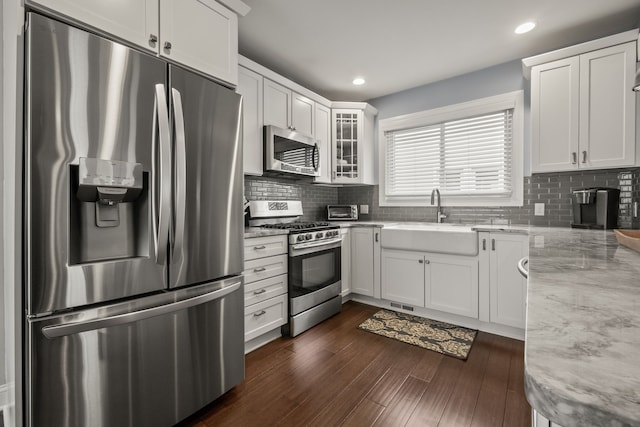 kitchen with appliances with stainless steel finishes, a sink, light stone countertops, glass insert cabinets, and white cabinets